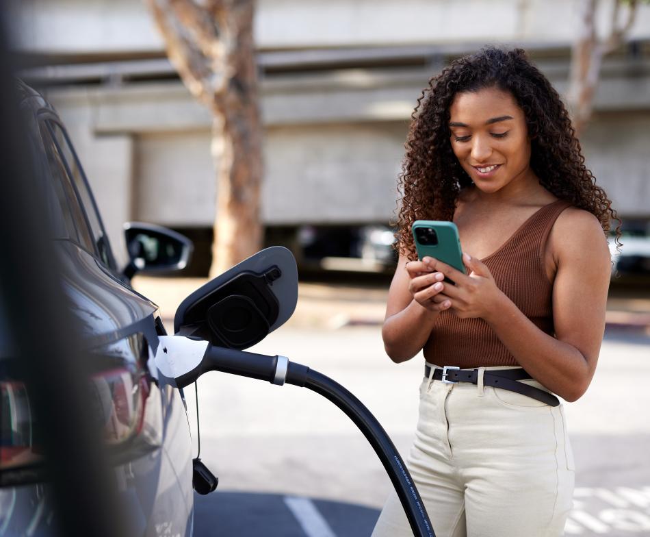 Woman charging her EV and looking at her phone